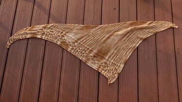 Gestricktes braun-beiges Dreieckstuch mit Zopfmuster auf Holzdielen