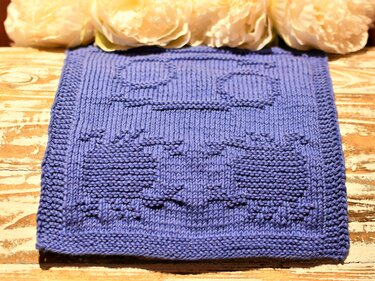Quadratisches blaues Stricktuch mit reliefartigem Fahrzeugmotiv auf Holzoberfläche