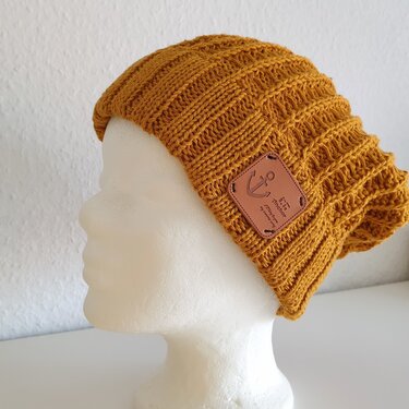 Senfgelbe gestrickte Mütze mit geripptem Muster und braunem Anker-Patch auf weißem Puppenkopf