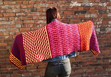 Rückenansicht einer Person, die ein farbenfrohes, gehäkeltes Patchwork-Tuch mit grafischen Mustern ausbreitet