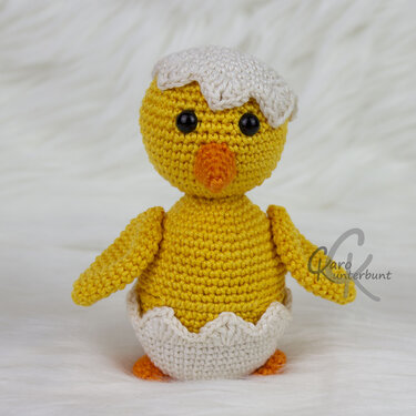 Gehäkeltes gelbes Küken mit weißer Eierschale auf hellem Hintergrund