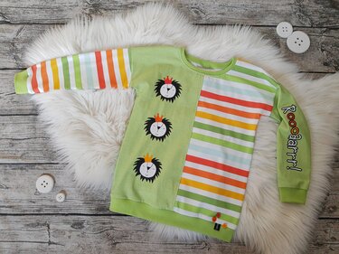 Grünes Kinder-Sweatshirt mit drei Löwenköpfen mit Krone, bunten Streifen und dem Schriftzug 'Roooaarr!' am Ärmel