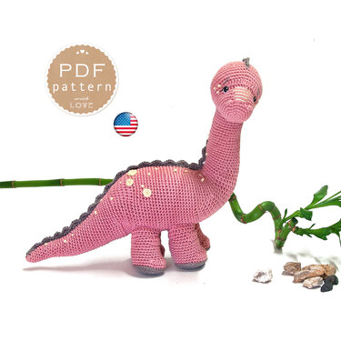 Pink crocheted amigurumi long-neck dinosaur with gray spine ridges and pale spots on a white background