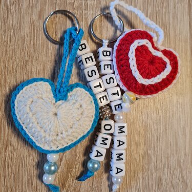 Zwei gehäkelte Herz‑Schlüsselanhänger (weiß‑blau, rot‑weiß) mit Perlen und Buchstabenwürfeln ‚BESTE OMA‘ und ‚MAMA‘
