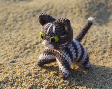 Close-up of a brown and white striped crochet amigurumi cat with green eyes