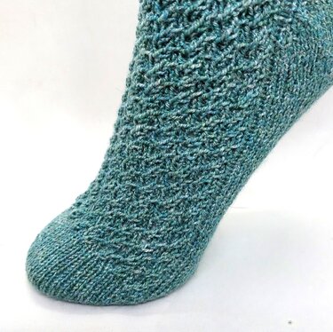 Nahaufnahme einer petrolfarbenen gestrickten Socke mit feinem Strukturmuster an Spitze und Spann