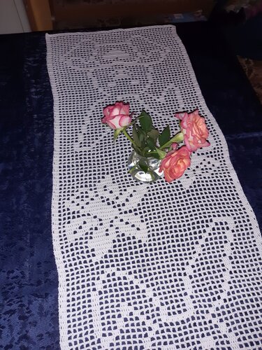 Weißer Filet-Tischläufer mit floralem Muster und Glasvase mit rosa Rosen
