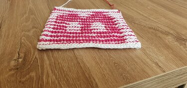 Gestrickte Maschenprobe in Pink und Weiß mit Herzmotiv auf Holzuntergrund