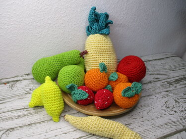 Gehäkelte Amigurumi-Früchte auf einem Holzteller mit Ananas, Banane, Zitrusfrüchten und Erdbeeren.