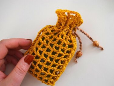 Gehäkeltes senfgelbes Säckchen mit Netzmuster, Kordelzug und Holzperlen, von Hand gehalten