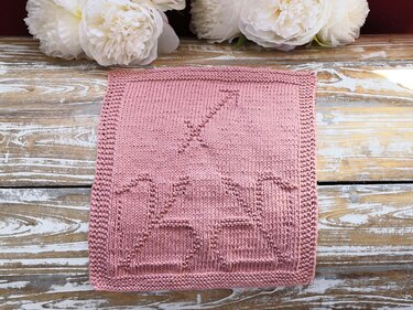 Zartes altrosa Strickpanel mit reliefierten Mustern und krausgestricktem Rand auf Holzuntergrund, weiße Blumen im Hintergrund