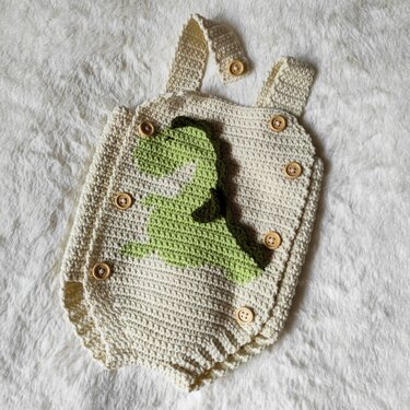 Cream crocheted baby romper with green dinosaur motif and wooden buttons