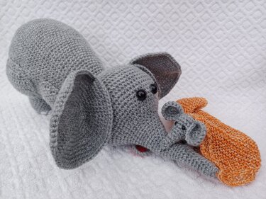 Gehäkelter grauer Elefant mit großen Ohren und kleinem Elefantenbaby, neben orangefarbenem Häkelstück