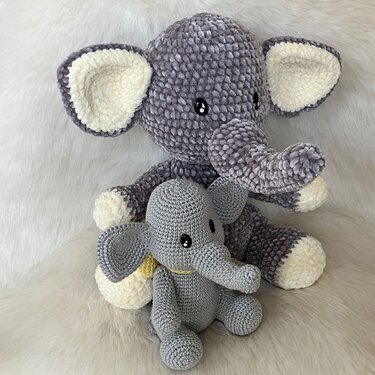 Zwei graue Amigurumi-Elefanten: ein großer plüschiger Elefant und ein kleiner fein gehäkelter Elefant auf hellem, flauschigem Untergrund