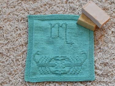 Türkises quadratisches Stricktuch mit Skorpion-Motiv und zwei Seifenstücken auf hellem Teppich