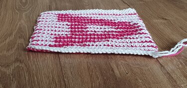 Rechteckiges Strickstück mit eingestricktem Herzmuster in Pink und Weiß auf Holz