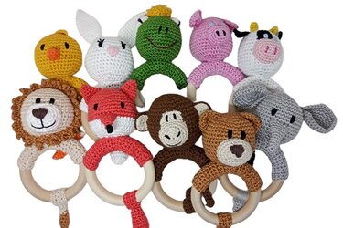 Mehrere gehäkelte Baby-Rasseln mit Holzringen in Tierform (Ente, Hase, Frosch, Schwein, Kuh, Löwe, Fuchs, Affe, Bär, Elefant) auf weißem Hintergrund