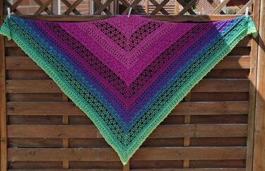 Gehäkeltes Dreieckstuch mit Farbverlauf in Pink, Lila, Blau und Grün an einem Holzzaun