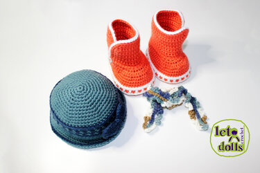 Orange crocheted booties with white trim, a teal crocheted hat, and a small multicolored crochet accent on a white surface.