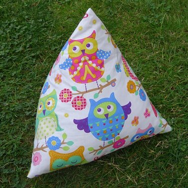 Dreieckiges Kissen mit bunten Eulenmotiven und kleinen Zierknöpfen auf Gras