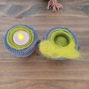 Zwei runde gehäkelte Dekoelemente, links mit LED‑Teelicht, rechts mit gelber, flauschiger Füllung