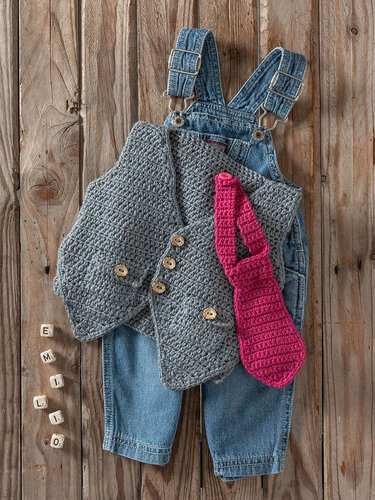 Gehäkelte graue Babyweste und pinke Krawatte auf blauer Jeans-Latzhose, arrangiert auf einem Holzboden.