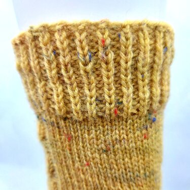 Gestrickter Sockenbund in Senfgelb mit bunten Tweed‑Sprenkeln, Rippenstruktur