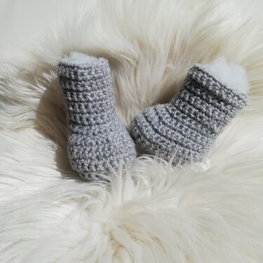 Gehäkelte graue Babyschuhe mit sichtbarer Maschenstruktur auf hellem Fell