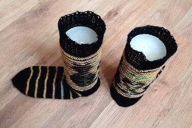 Gestrickte Socken und Stulpen mit mehrfarbigen Streifen, schwarzem Bündchen und Spitzenkante, teils auf Formen, teils flach auf Holzboden