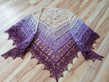Openwork crochet triangle shawl with graduated cream to purple color and scalloped lace motifs