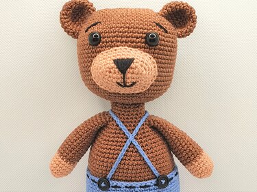 Gehäkelter Amigurumi-Teddybär in Braun mit heller Schnauze und blauer Latzhose