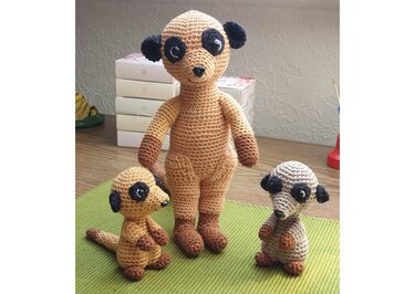 Drei gehäkelte Erdmännchen in verschiedenen Größen auf grüner Unterlage.