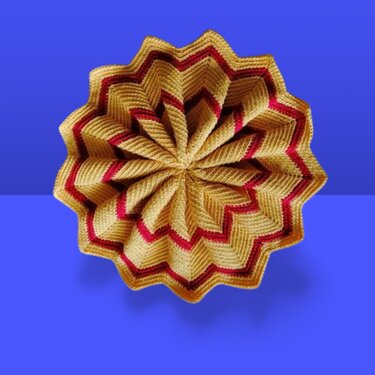 Gehäkelter sternförmiger Faltstern in Gold und Rot vor blauem Hintergrund