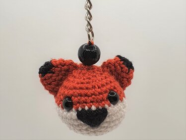 Gehäkelter Fuchskopf‑Schlüsselanhänger in Orange, Weiß und Schwarz an einer Metallkette.