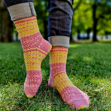 Pink-gelb gestreifte handgestrickte Socken mit Lochmuster auf grünem Gras.