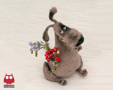 Brown crocheted amigurumi dog plush with floppy ears holding red berries and small purple flowers.