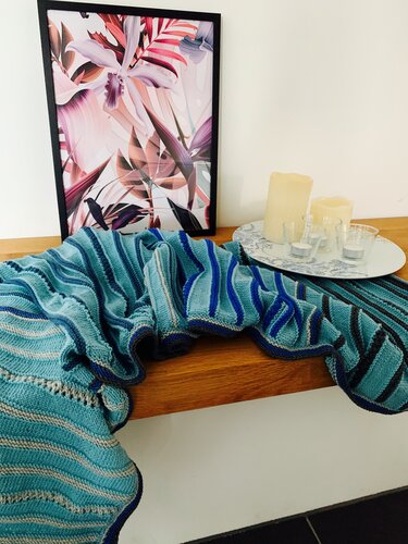 Nahaufnahme eines gestrickten Schals mit variierenden Streifenbreiten in Türkis- und Blautönen und dunkler Kante