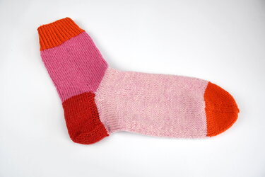 Gestrickte Socke flach gelegt in Rosa, Pink, Rot und Orange mit geripptem Bündchen, roter Ferse und oranger Spitze