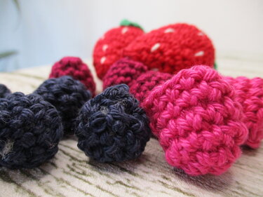 Nahaufnahme gehäkelter roter Erdbeeren und dunkler Beeren