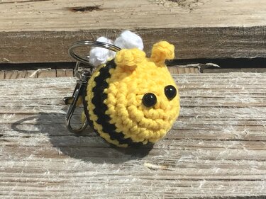 Gehäkelter Bienen-Schlüsselanhänger gelb und schwarz mit Schlüsselring auf Holzuntergrund