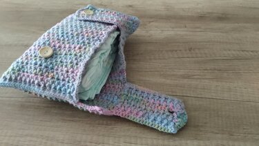 Gehäkelte Wickeltasche in Pastellfarben mit zwei Holzknöpfen, gefüllt mit Windeln auf hellem Holzuntergrund