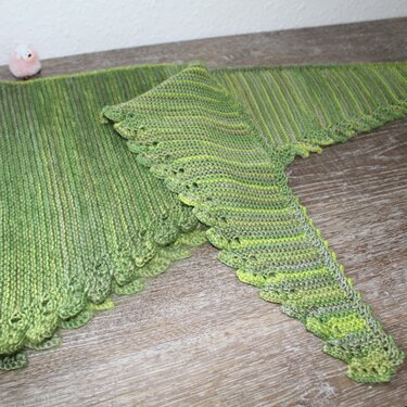 Grünes gestricktes Dreieckstuch mit Spitzenkante auf Holztisch