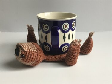 Gehäkelter Faultier-Untersetzer in Braun mit Tasse auf dem Rücken