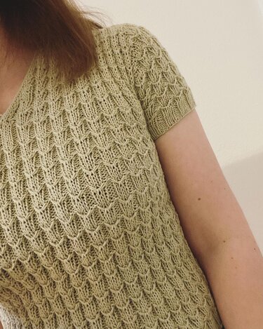 Close-up of a sage green short-sleeved knitted top with textured stitch pattern and V-neckline.