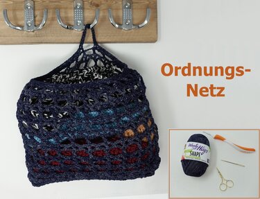 Dunkelblaues gehäkeltes Ordnungsnetz mit farbigen Akzenten an einer Garderobenleiste, daneben Garn und Häkelnadel