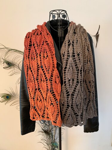 Zwei gehäkelte Schals mit Blattspitzenmuster in Orange und Braun über einer schwarzen Jacke drapiert