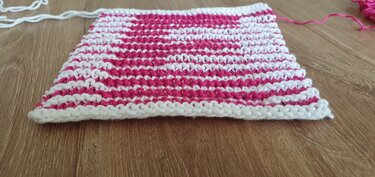 Zweifarbige Strickprobe mit pinken und weißen Reihen auf Holz, losen Garnenden
