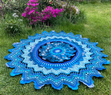 Runde gehäkelte Mandala-Decke in Blautönen auf Rasen