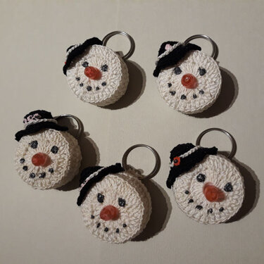 Fünf gehäkelte Schnemann‑Schlüsselanhänger mit schwarzen Hüten und Metallringen