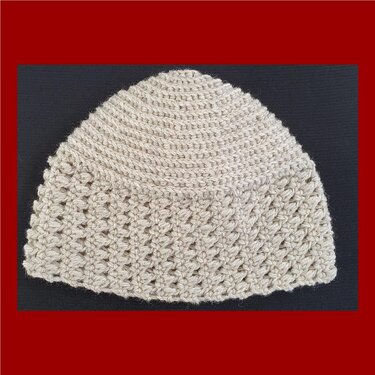 Hellbeige gehäkelte Beanie mit strukturiertem Rand vor dunklem Hintergrund